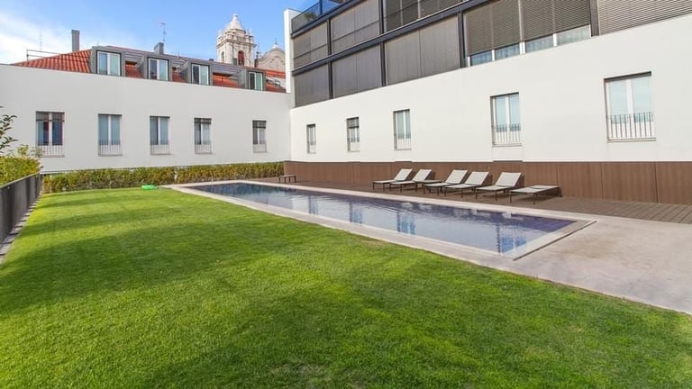 Modern rooftop pool with lounge chairs on manicured lawn surrounded by urban apartment buildings